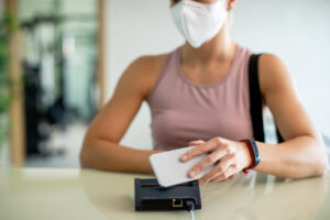 woman in mask tapping phone on touchless device