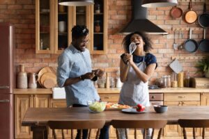 Happy energetic young african american family couple having fun, preparing food together.