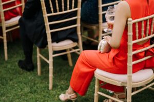 Woman in a red suit sits on a chair among the guests on the lawn. Back view. High quality photo