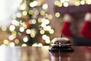 Christmas travel. Silver vintage bell on reception desk of guesthouse and color shining garland on christmas tree on background. Hotel, restaurant.