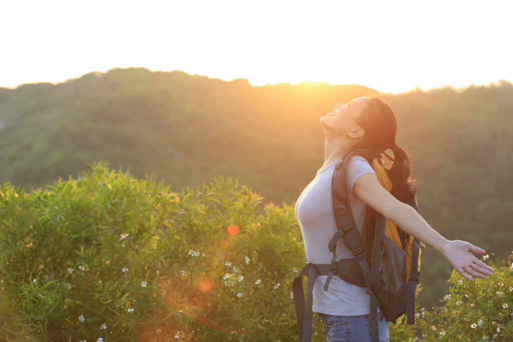 Happy woman, with outstretched arms, is hiking during the sunrise on a mountain peak