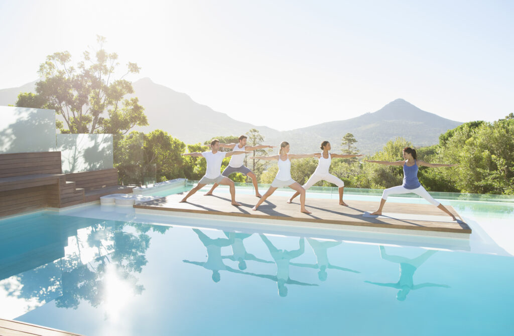 Yoga instructor teaches yoga class by the poolside with a mountainous view in the background