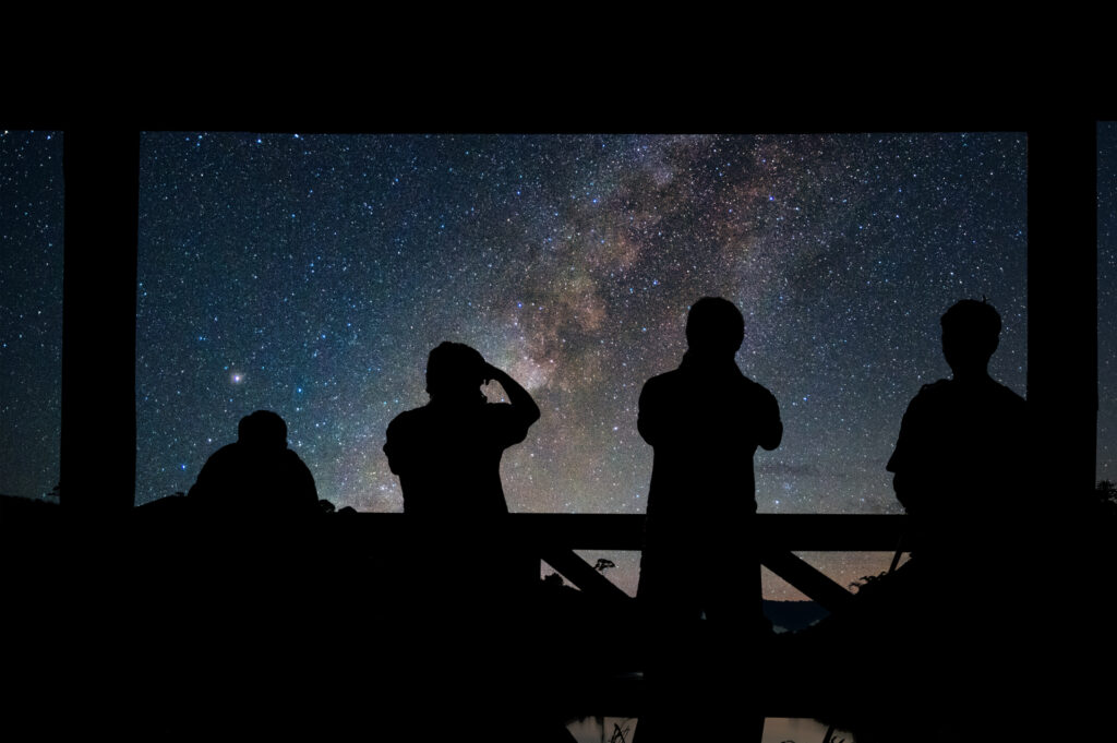 Travelers stargazing under the Milky Way galaxy, part of an astrology-inspired travel experience.