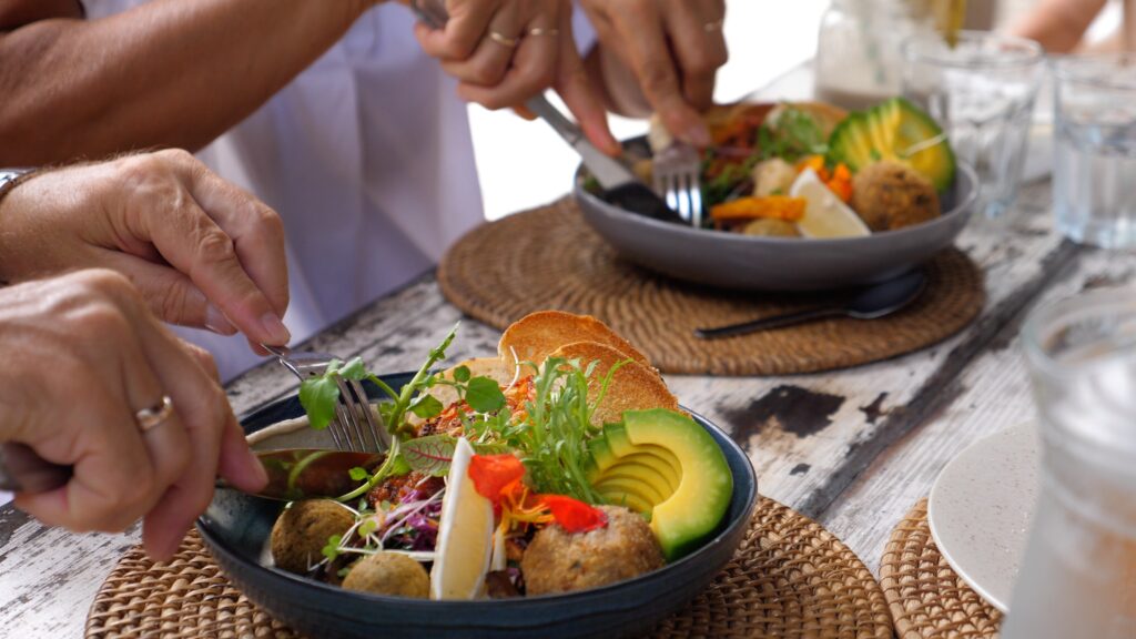 Close-up of hands enjoying a fresh plant-based meal with avocado, greens and grains, reflecting the Blue Zone diet of healthy, longevity-focused eating.