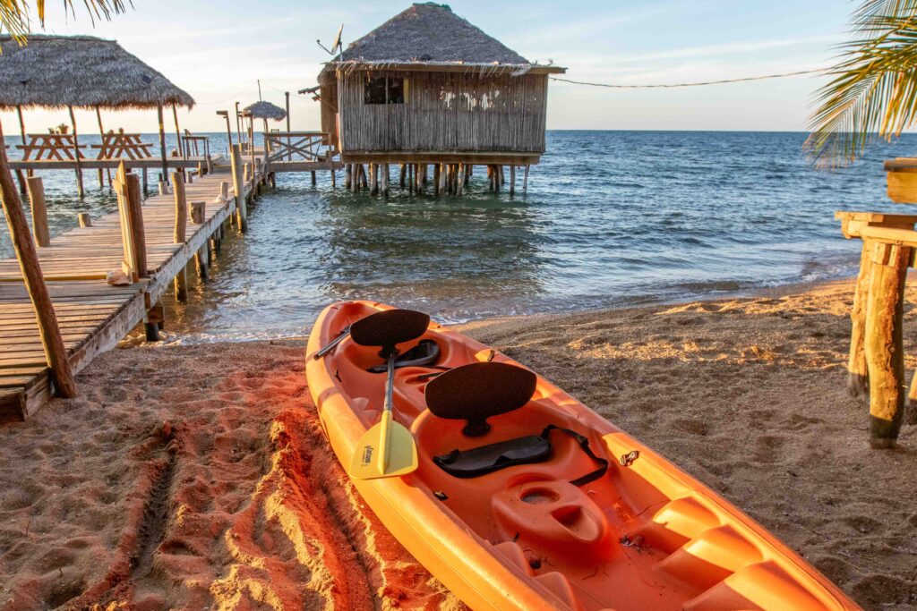 Orange kayak sitting between the beach and sand, nestled beside a dock.