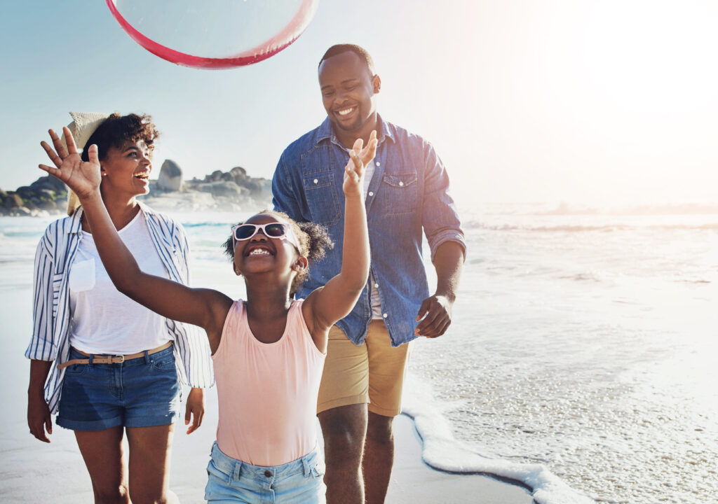 Family enjoying a budget travel beach vacation by walking the sandy beach.