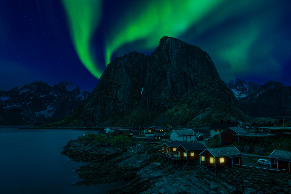 Northern lights over mountains and cabins, a popular astrotourism destination for travelers seeking night sky wonders.