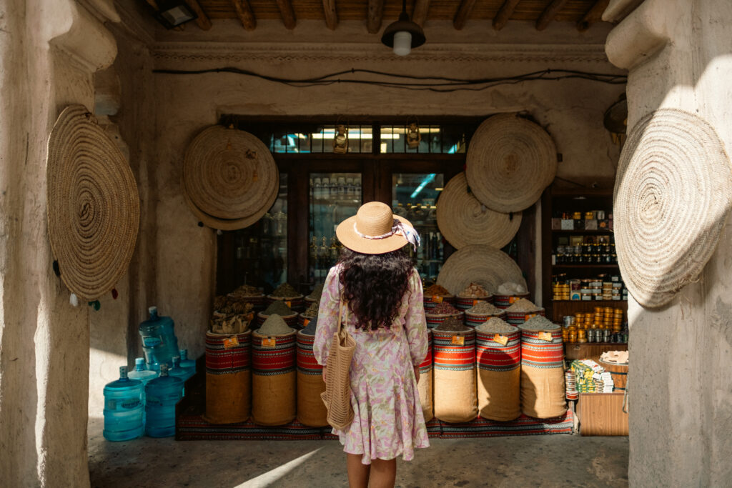 A woman dressed in vacation attire, with her back facing the camera, staring at an impressive display of herbs and spices. 