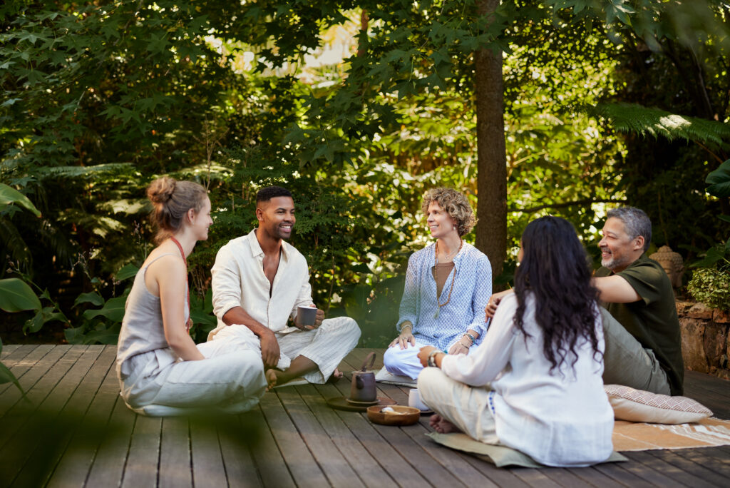 A circle of people in a group, meditating around a pot of tea while participating in transformational travel. 