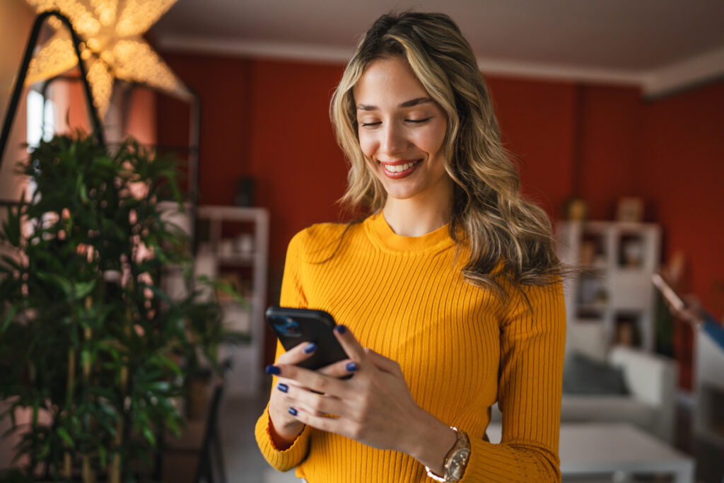 A woman happily peering into her phone while viewing an email triggered by email marketing automation. 