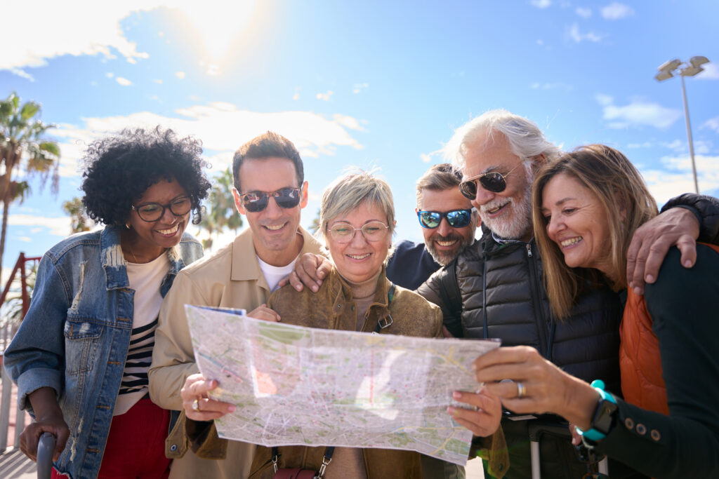 A group of traveling friends, gazing at a map with smiles on their faces, while standing outside in the sun.