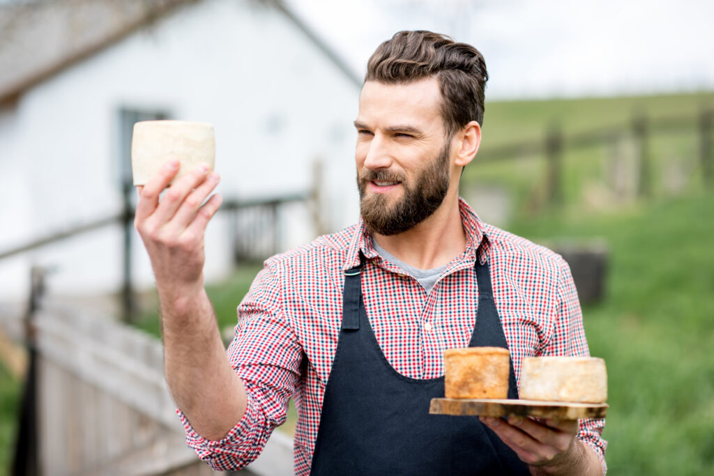 A young farmer in an apron checking the quality of cheese outdoors on a rural farm.