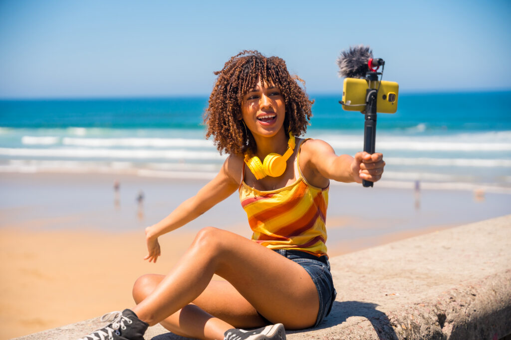 Young female vlogger creating social media content for her followers while enjoying a sunny day at the beach.