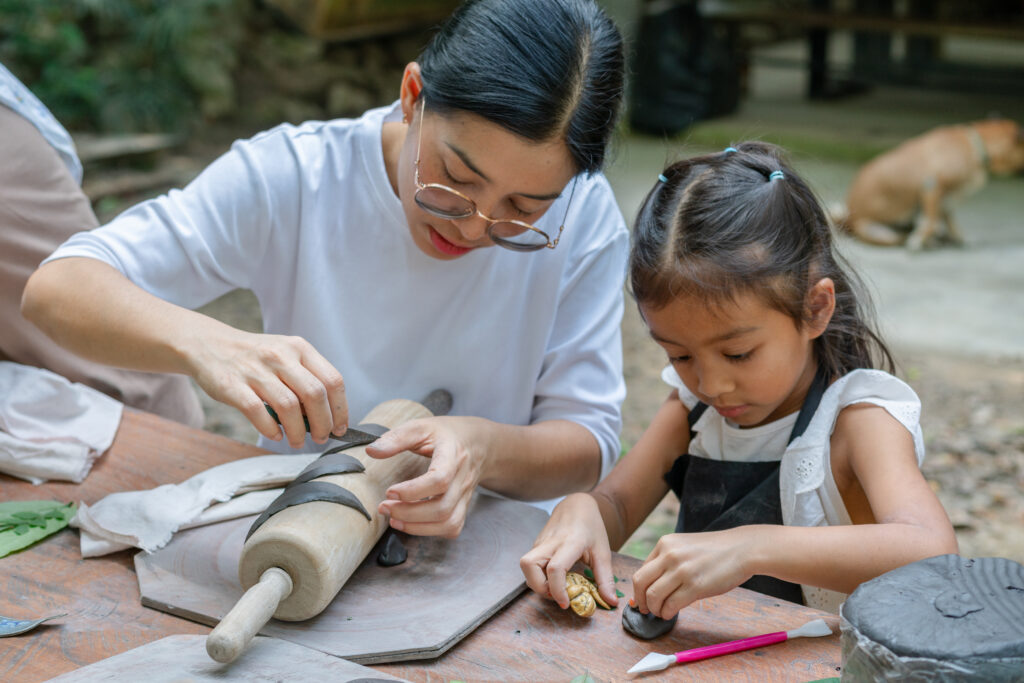 A mother and her young daughter, during their family travel, molding clay together during a pottery workshop.