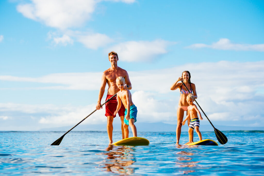 Family of four, with two children, paddling on two paddle boards on the ocean during a sunny day.