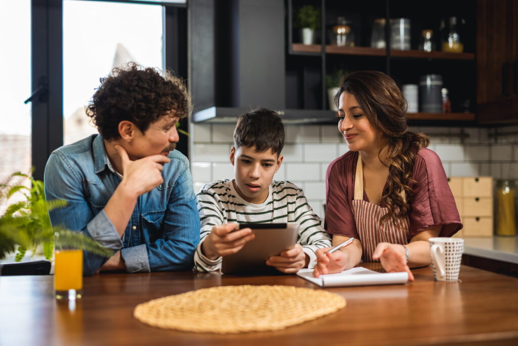 Two parents and their son, viewing an Ipad happily, while sitting in their kitchen planning their family travel.