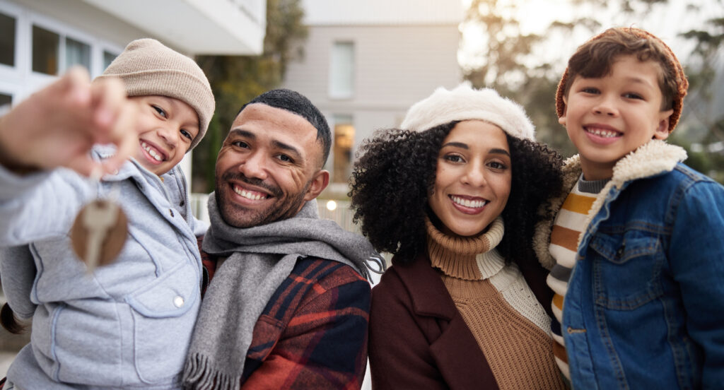 A happy family, parents and their two children, holding up keys towards the camera while smiling during winter.
