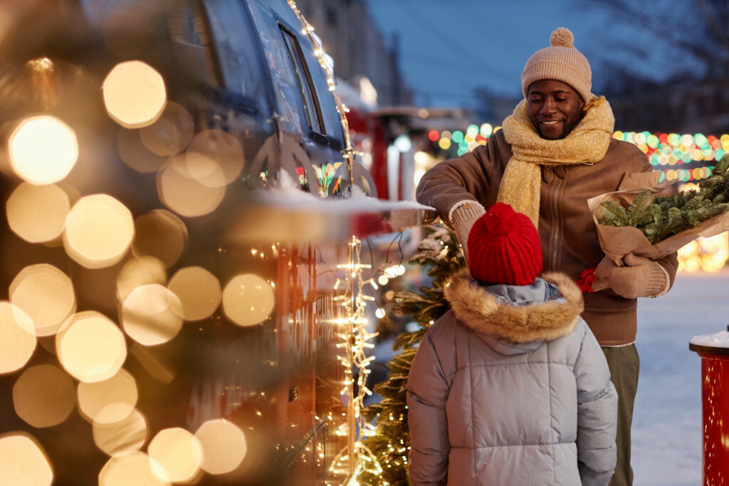 A happy father and daughter buying snacks and holiday decorations while standing near festive lights during a family getaway. 